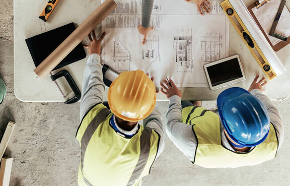 Top view of construction works gathered around a table covered in blueprints