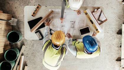 Top view of construction works gathered around a table covered in blueprints