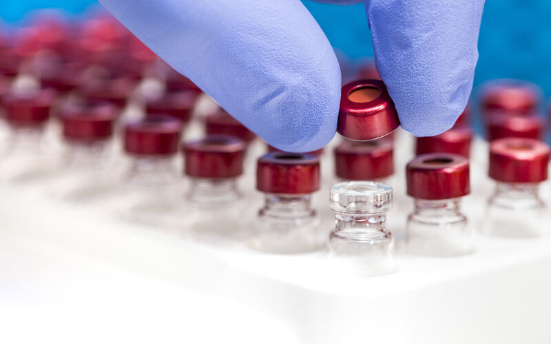 A gloved hand arranges test tubes in a lab