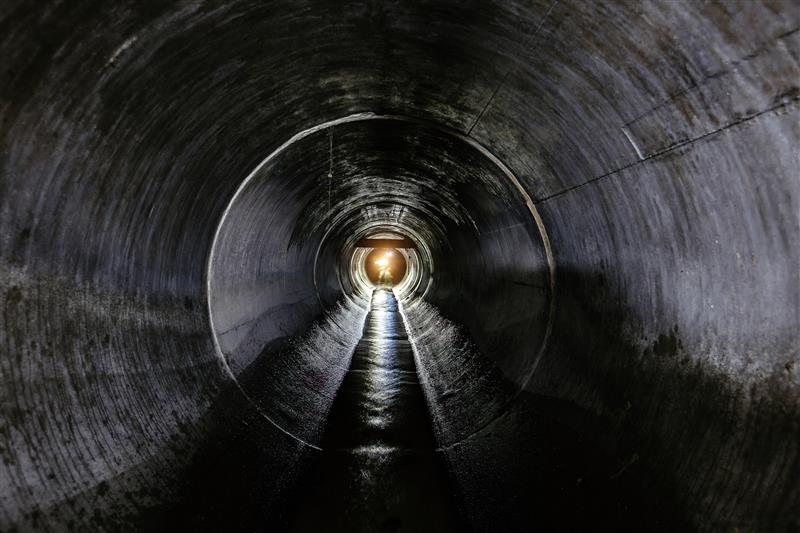 View looking through a long, concrete tunnel with light visible at the far end.