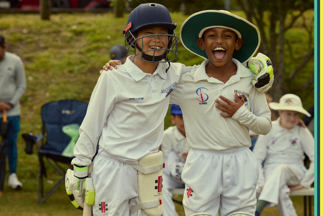 Two boys in cricket gear smiling and laughing in an embrace 