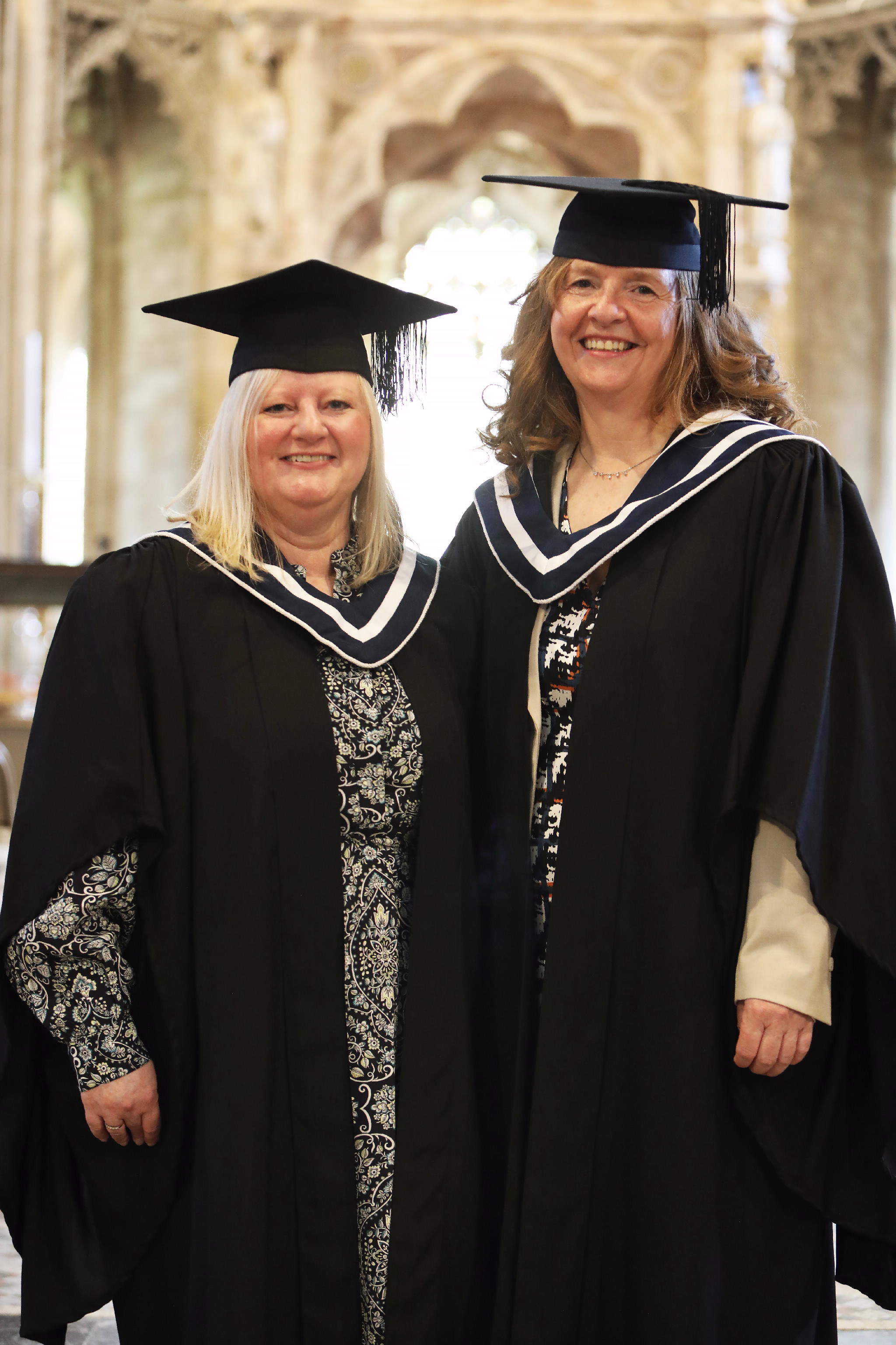 Two female graduates posing and smiling indoors