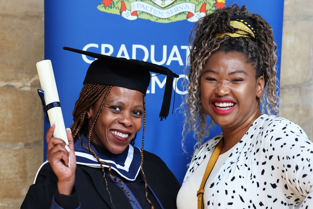 Two women, one in a cap and gown holding a diploma scroll