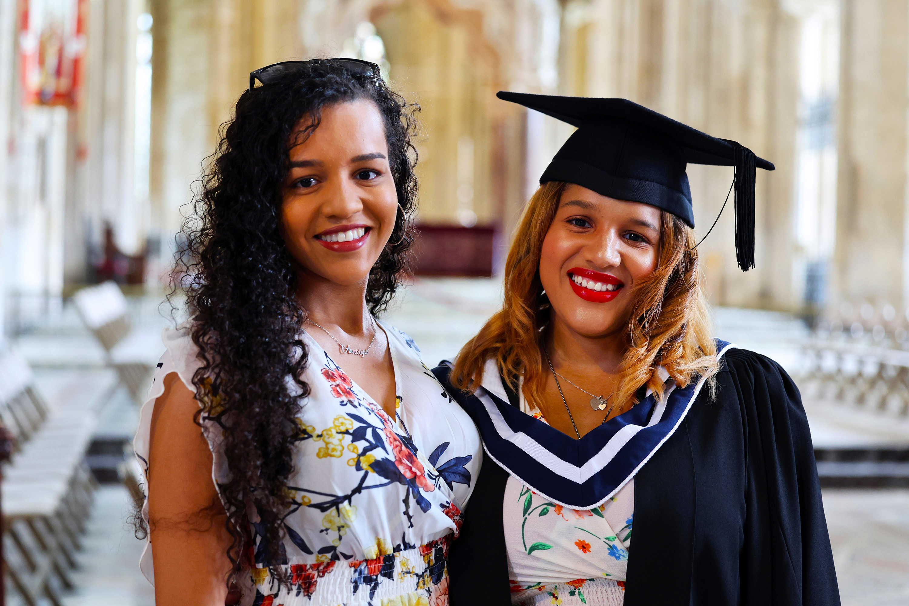 Two women smiling for a photo, one wearing a cap and gown