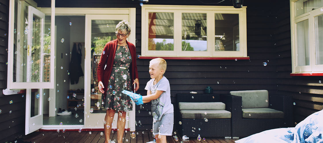 A senior white woman and her grandson play with a bubble maker on her porch