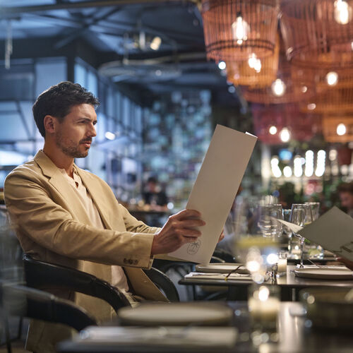 Man in a beige suit has trouble reading restaurant menu
