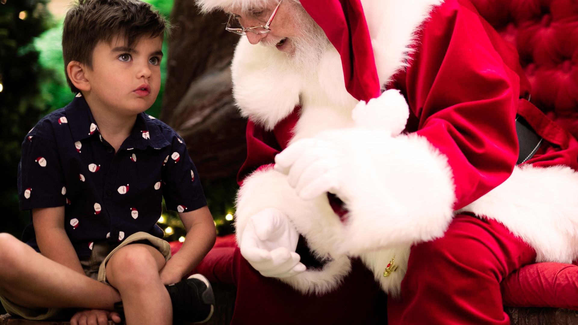 Santa leans in and gestures with his hands as a child sits beside him in a quiet Sensitive Santa session 