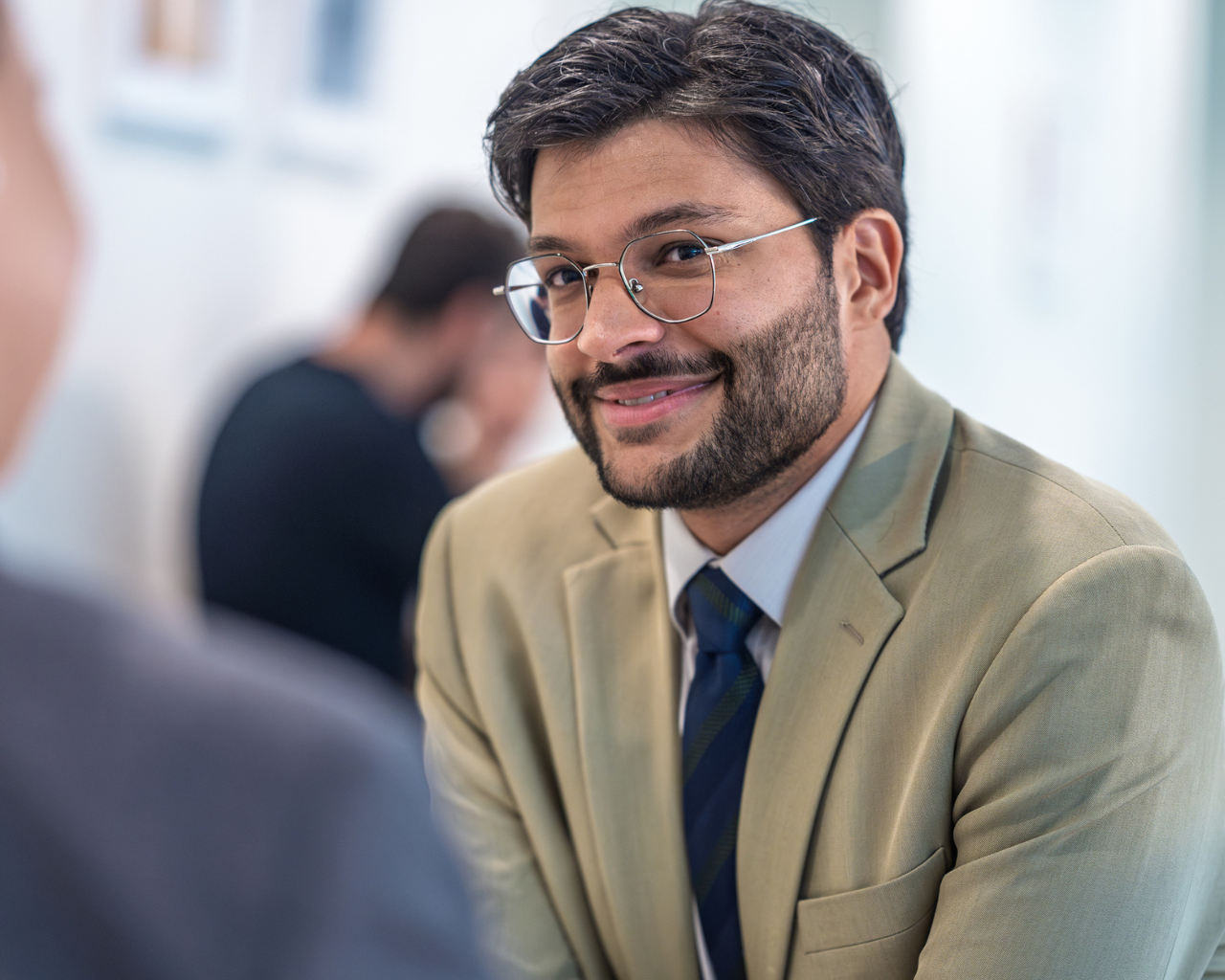 man in corporate attire and glasses smiling