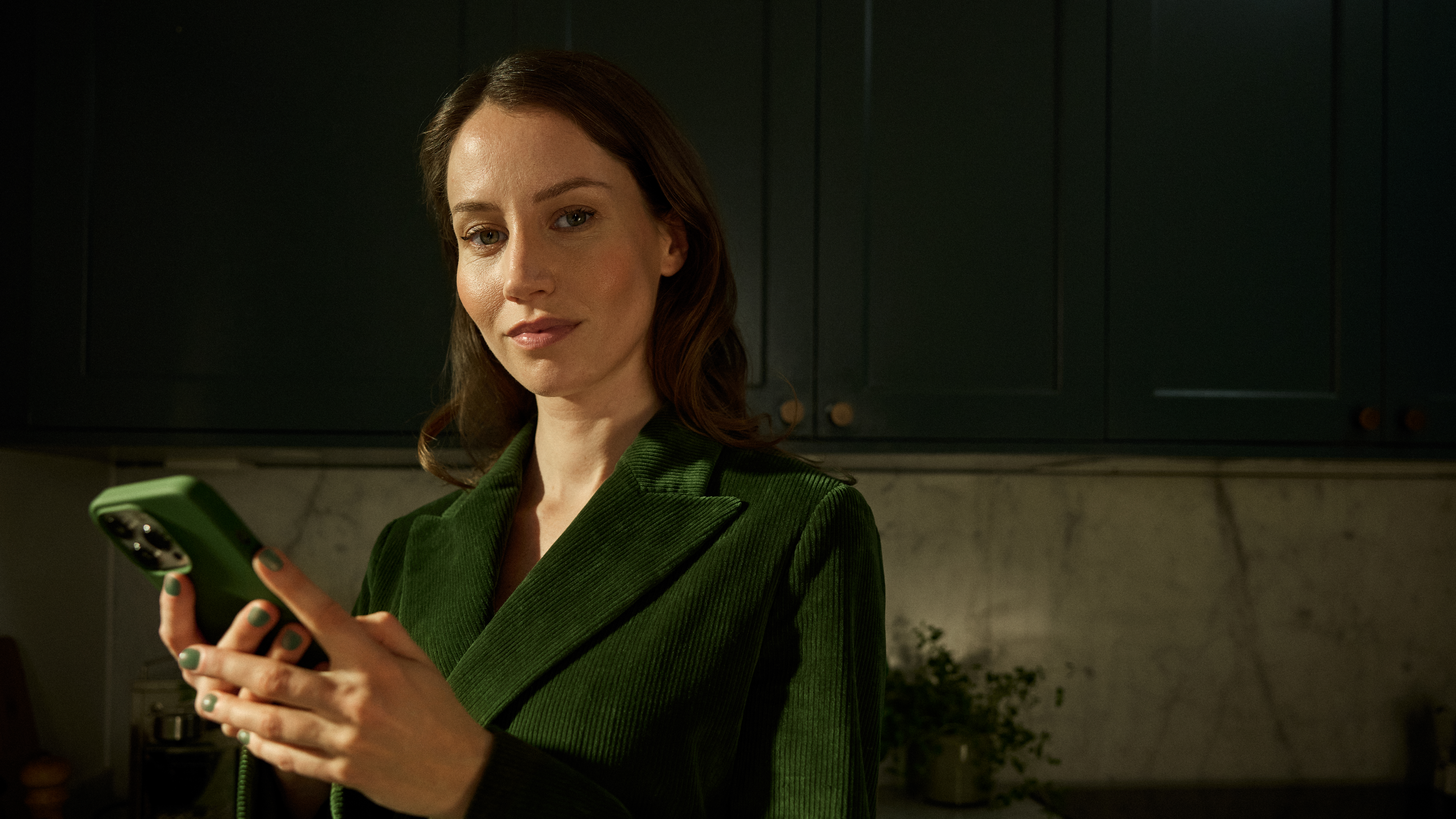 Kvinna med mobiltelefon som tittar på kameran. I mobilen handlar hon med fonder.