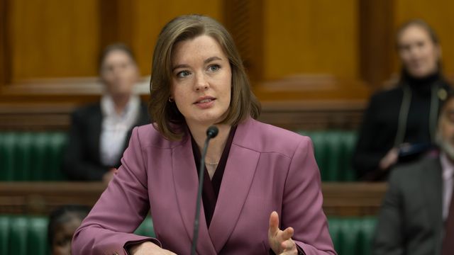 Amy James-Kelly as Jennifer Bevan speaking at a hearing, wearing a pink blazer