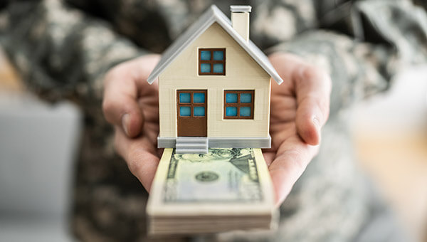 military personnel holding a stack of money and house model