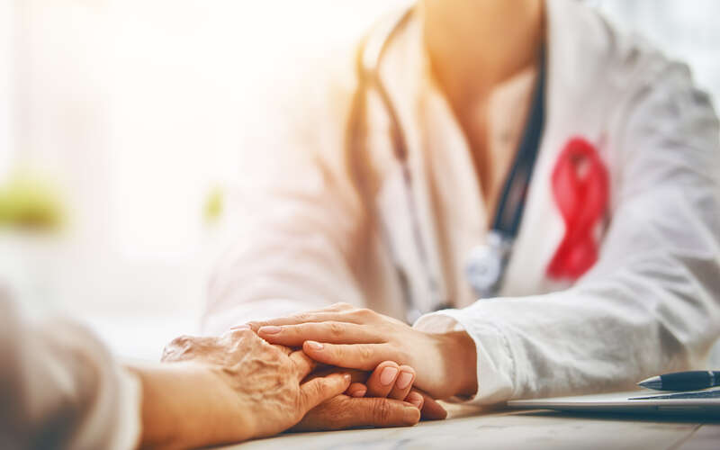 Breast cancer health care provider in white coat with stethoscope and pink ribbon holds hands with a patient