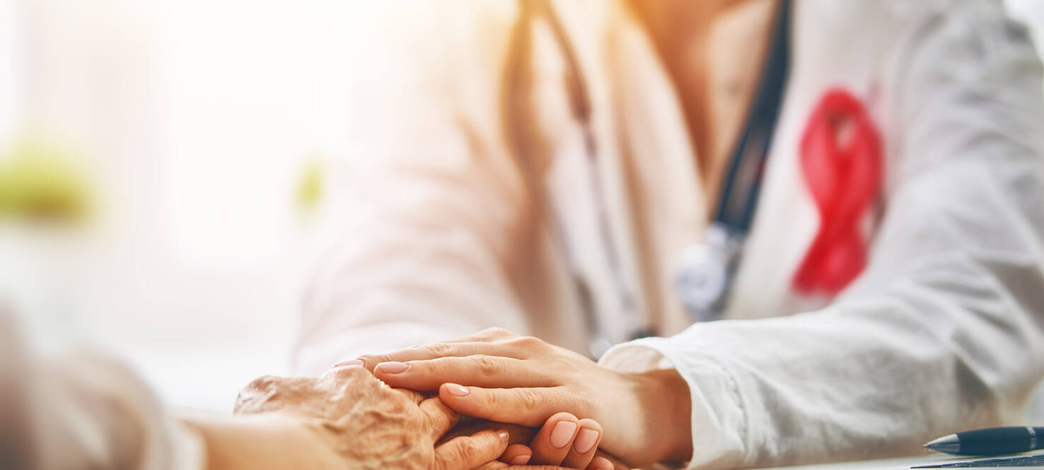 Breast cancer health care provider in white coat with stethoscope and pink ribbon holds hands with a patient