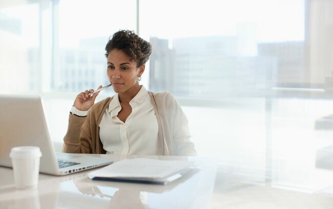 Business woman sitting at a desk in front of a window looking at a laptop 