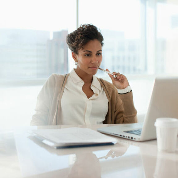 Business woman sitting at a desk in front of a window looking at a laptop 