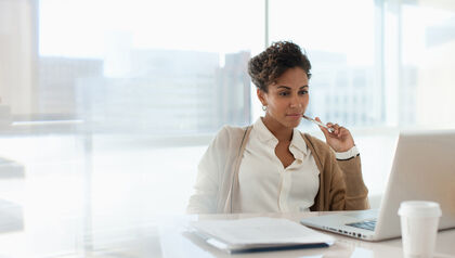 Business woman sitting at a desk in front of a window looking at a laptop 