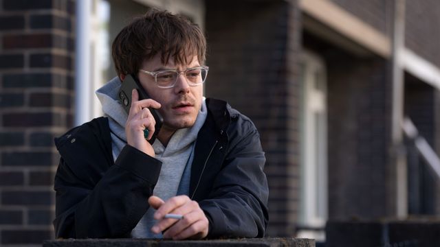 Charlie Heaton as Jim Dycker speaking on a phone outside wearing glasses and a hoodie