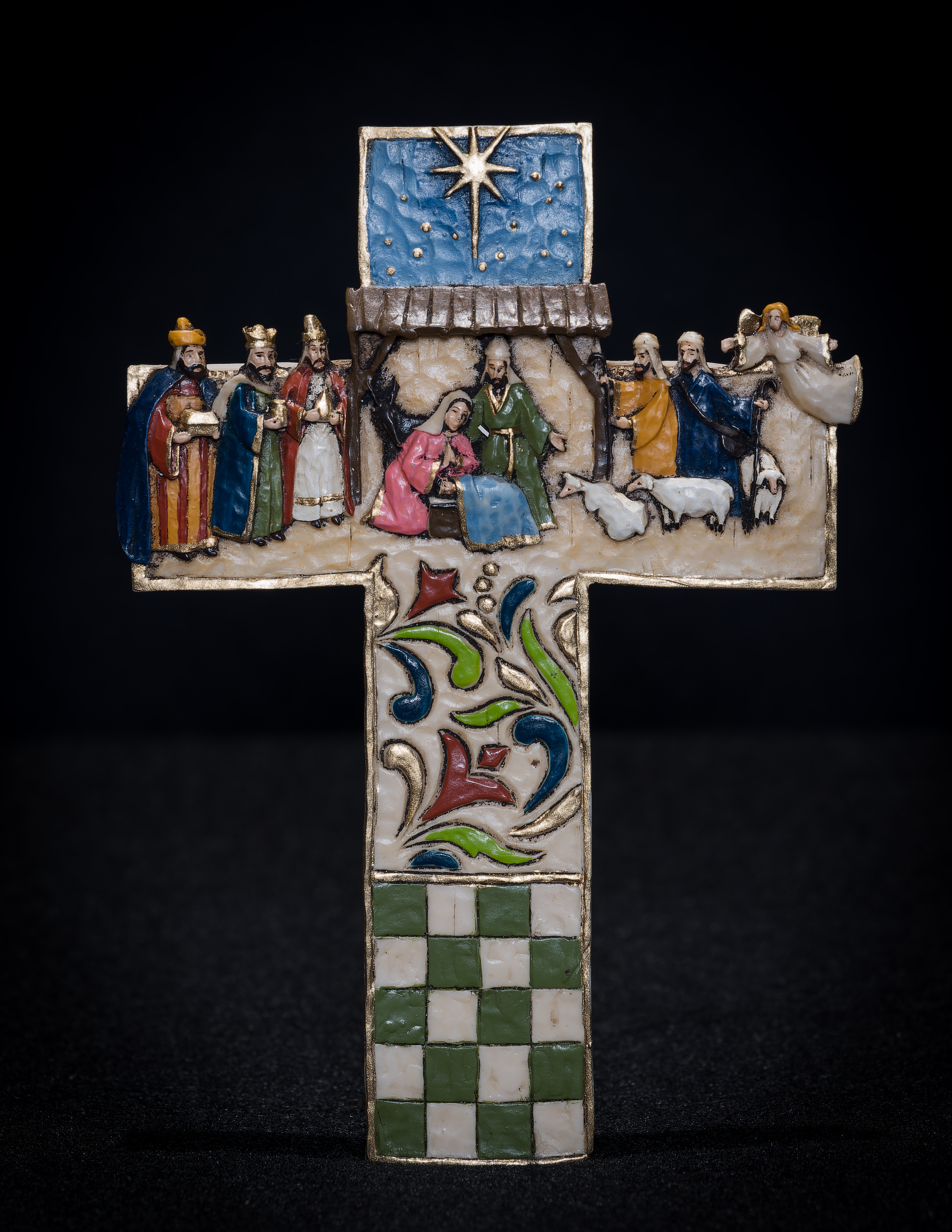 Nativity scene on a cross, with the Holy Family and donkey beneath the stable, and 3 Magi, 2 shepherds, an angel, and 3 sheep on the stable sides. 