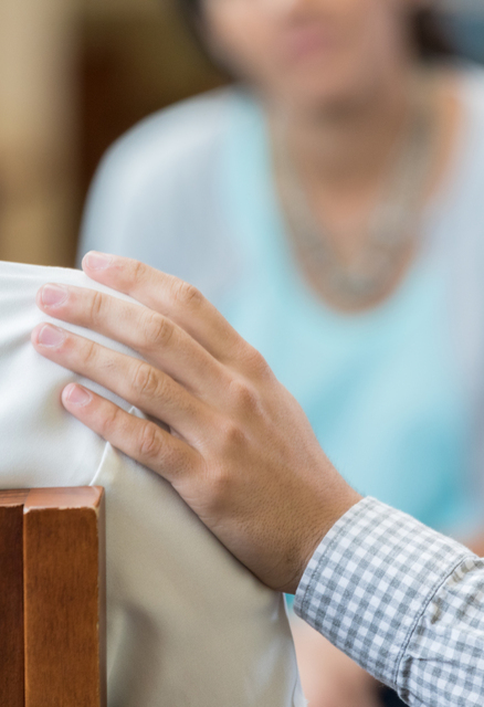 A man places a hand on another person's shoulder. Offering comfort. 