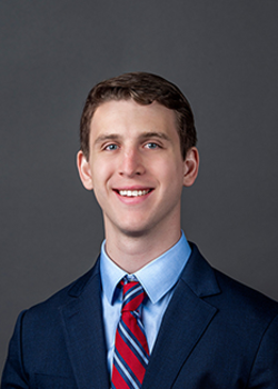 Headshot of Diego Zesati, who smiles while wearing a dark blue suit and a red and blue striped tie