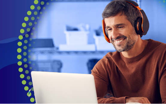 A man with a beard, wearing an orange and black headset, smiles while looking at a laptop screen. The image is overlaid with a vertical dotted yellow-green arc on the left side.