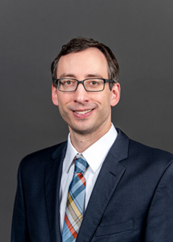 Headshot of Eric Eaton, who smiles while wearing a dark blue suit and a blue, yellow, and burnt orange plaid tie