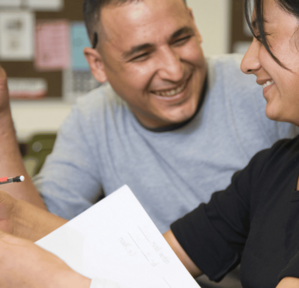 Two adults smiling while discussing finances and reviewing documents together.