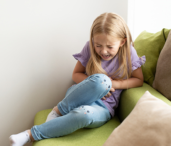 Deklica sedi na postelji zvita zaradi bolečin v trebuhu