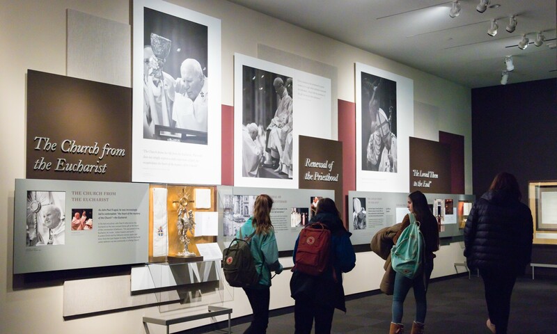 A group of individuals observing a gallery of Pope John Paul II images.
