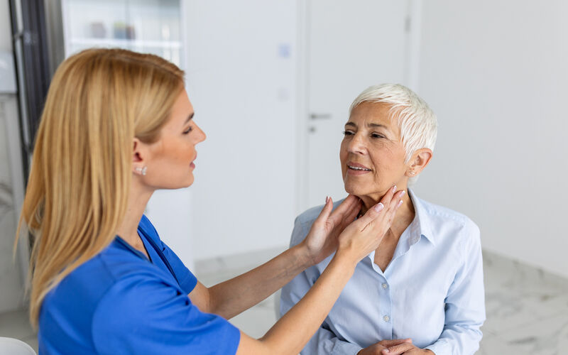 A female health professional exams another woman's neck during an exam.