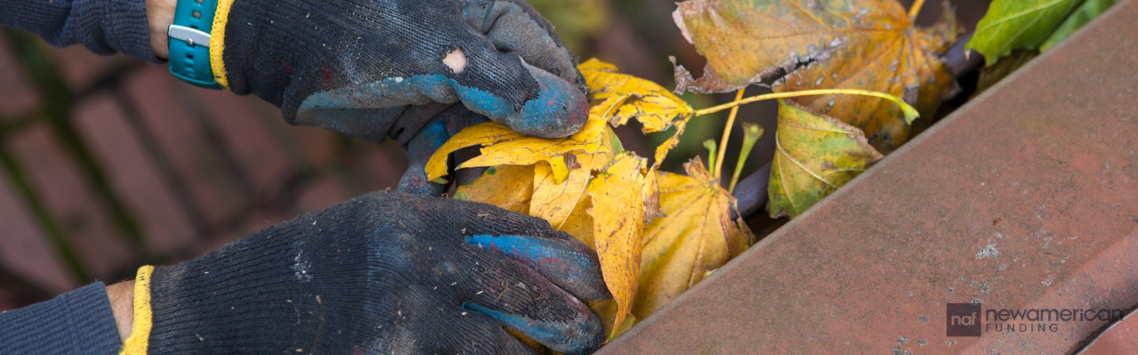 A person cleans out leaves from the gutters of a house