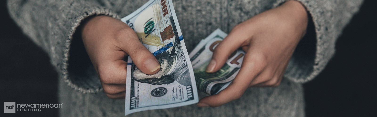 A person is holding several one-hundred dollar bills in their hands