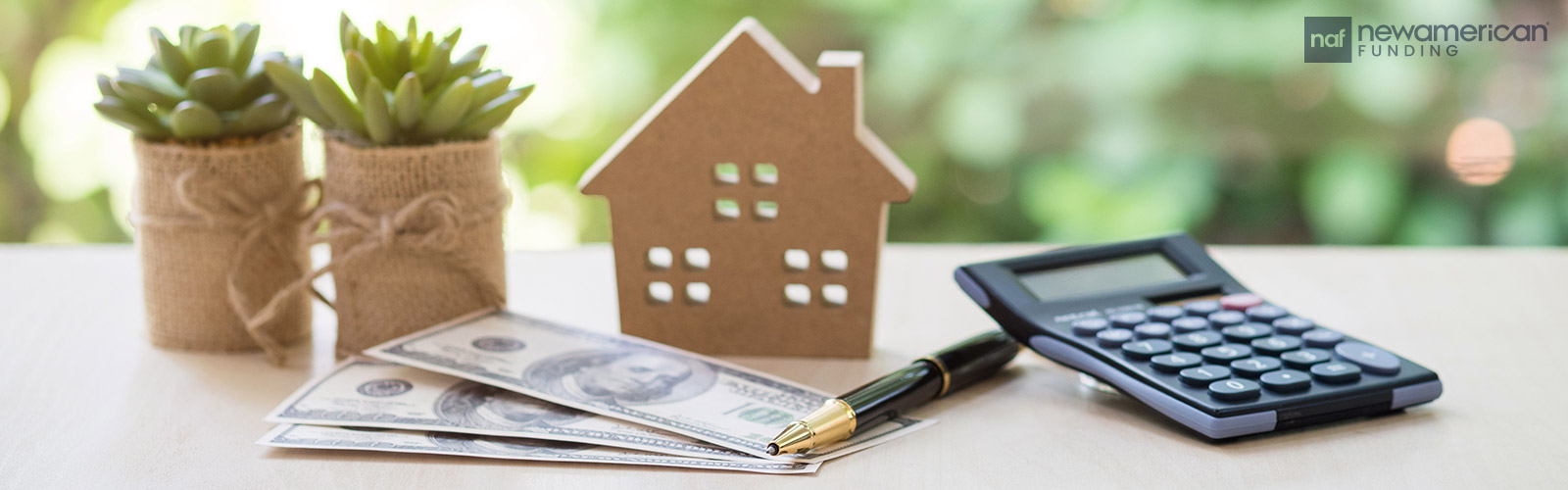 A desk with hundred dollar bills, a small model of a house, and some plants on it