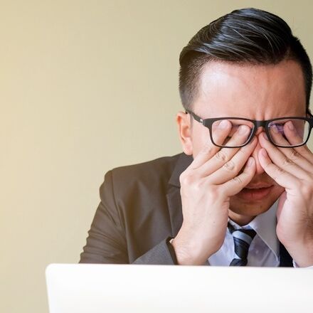 Uomo con gli occhiali che si strofina gli occhi mentre lavora al computer portatile