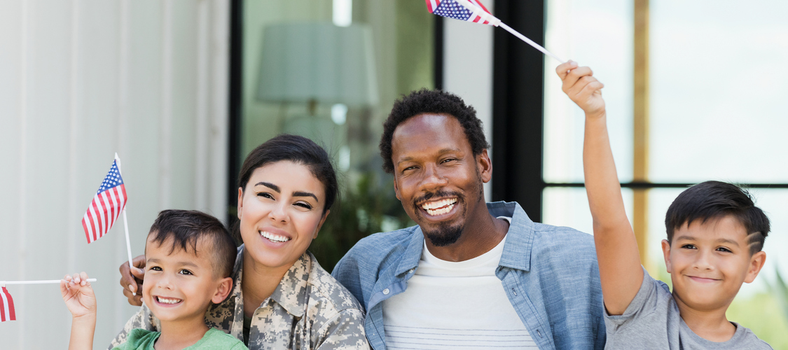 A woman in military clothing with a man and two small boys waving American flags.