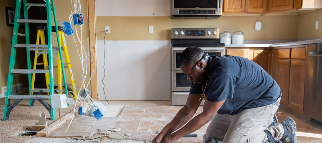 A man ripping up tiles in a kitchen that's being remodeled.