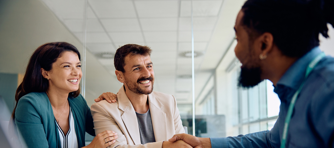 A couple sitting across the desk from a man and shaking his hand in an office.