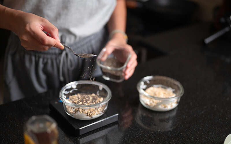 A woman's hand sprinkles chia seeds into a bowl of overnight oats, preparing a healthy and nutritious breakfast.
