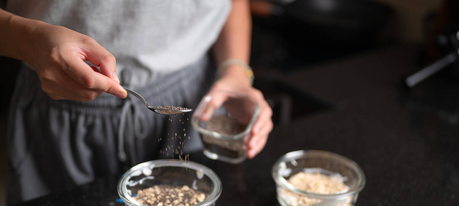 A woman's hand sprinkles chia seeds into a bowl of overnight oats, preparing a healthy and nutritious breakfast.