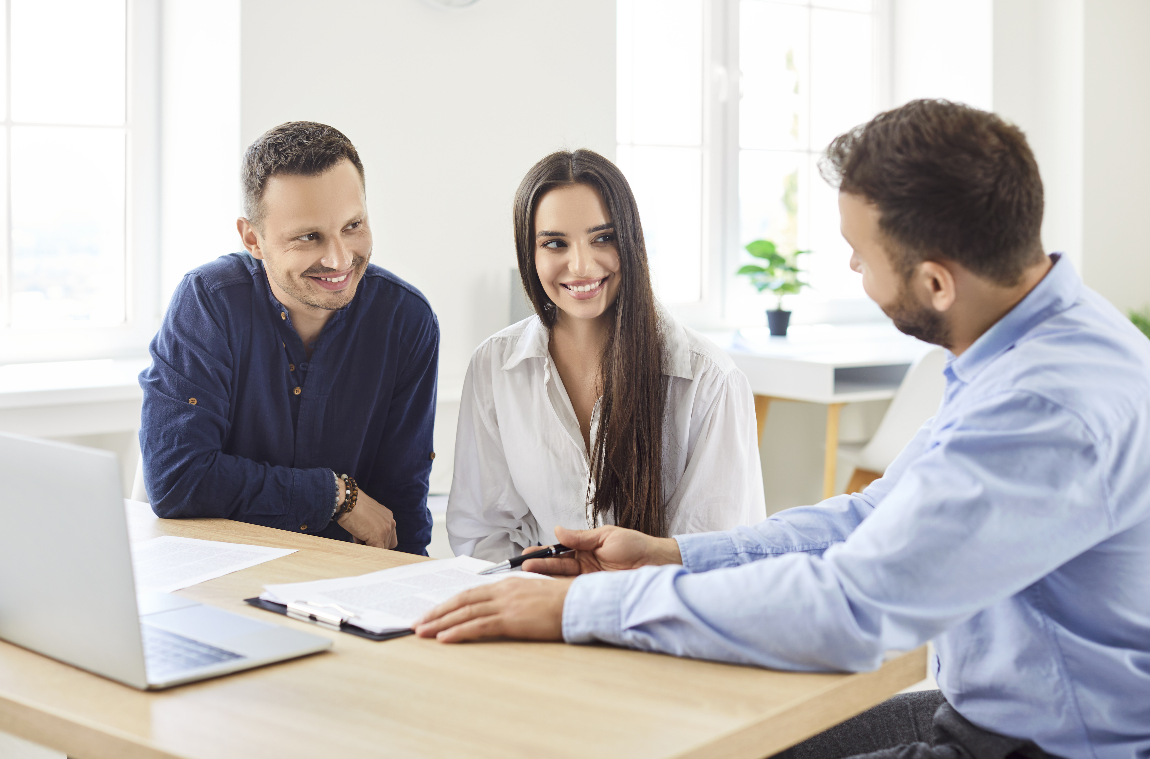 A couple sitting at a desk next to a man showing them some paperwork.