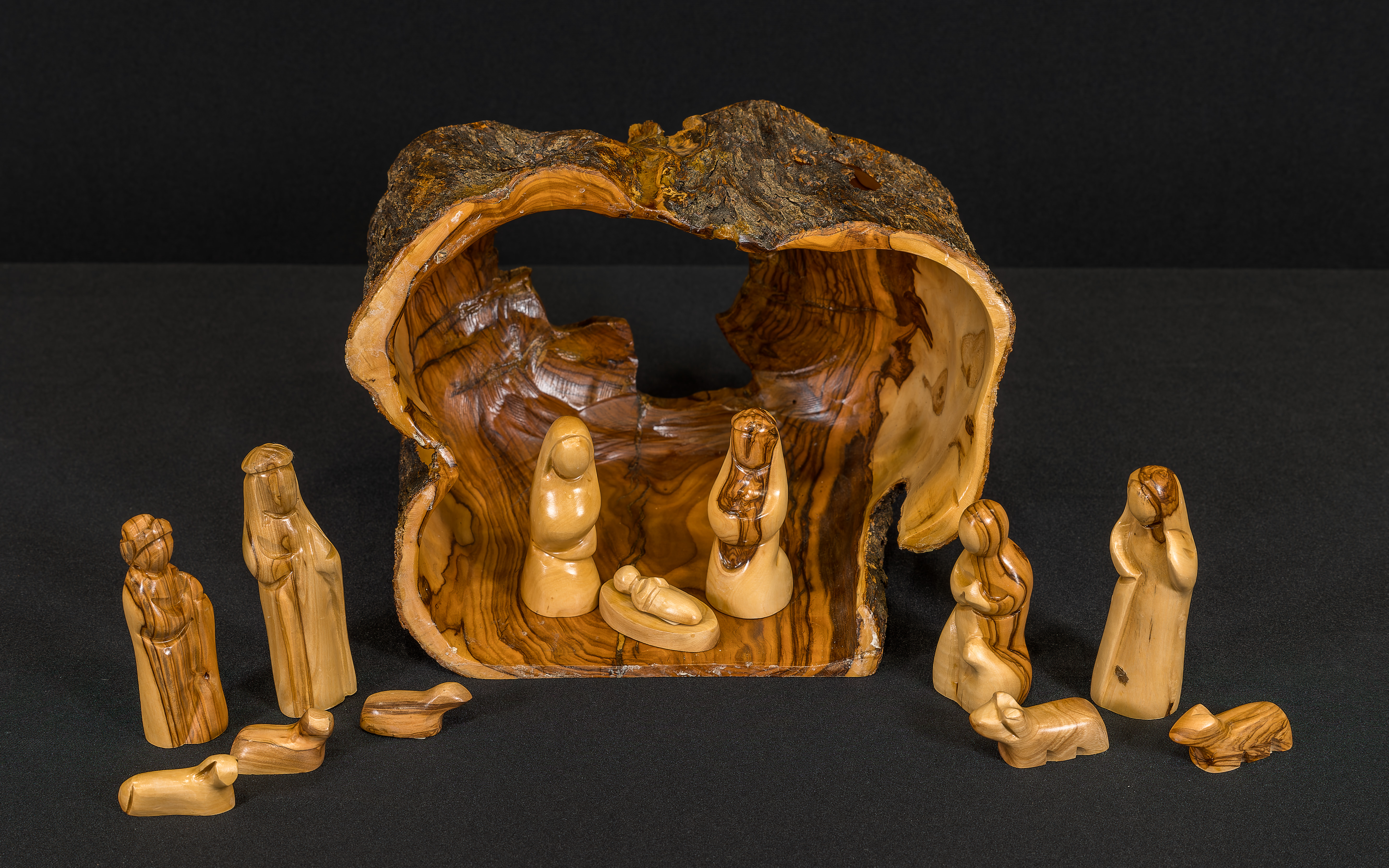 Olivewood carved Nativity with the Holy Family in a stable made from a hollowed-out log. Other figures of people and animals are outside the stable.