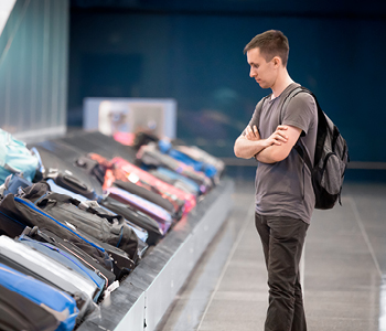 Potnik z zaskrbljenim izrazom stoji ob tekočem traku za prtljago na letališču.