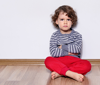 Kodrolas deček sedi na tleh s prekrižanimi nogami in prekrižanimi rokami kujavo zre v kamero.