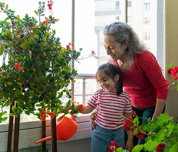Babica in vnučka zalivata rastlino na balkonu - babica uživa v življenju s pomočjo izplačila pokojninske rente