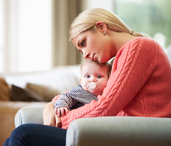 Simbolna fotografija za poporodno depresijo. Mlada mamica otožno pestuje dojenčka.