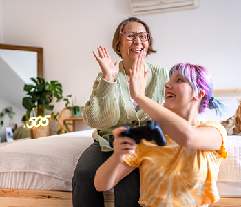 Prikupen medgeneracijski trenutek med babico in vnukinjo, ki igrata računalniške igrice.