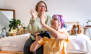 Prikupen medgeneracijski trenutek med babico in vnukinjo, ki igrata računalniške igrice.