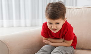 Deček na sliki se drži za trebuh in pači zaradi bolečin. Kako odpraviti bolečine v trebuhu pri otrocih je pogosto vprašanje staršev majhnih otrok.