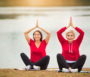Ženski po 50-tem se na nabrežju jezera ukvarjata z jogo.