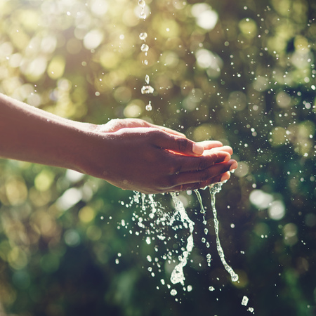 A person gently holds a water droplet in their hand, showcasing the fragility of nature.